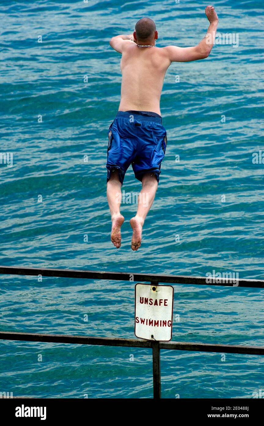 Male jumping off of a railing into water with sign saying Unsafe for