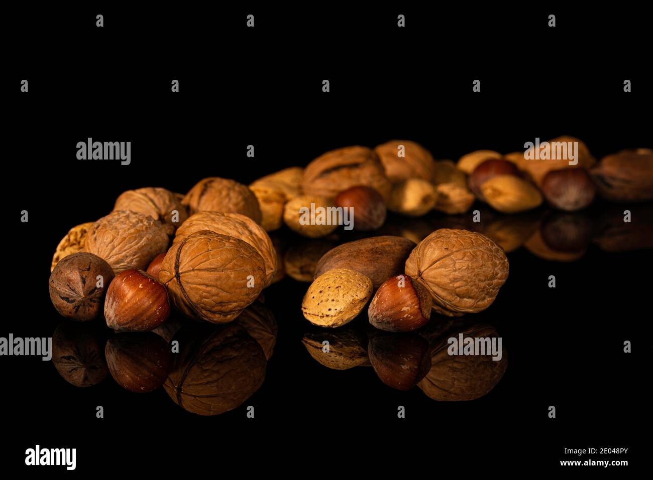 Walnuts, pecans, hazelnuts, almonds in shell on black reflective surface Stock Photo