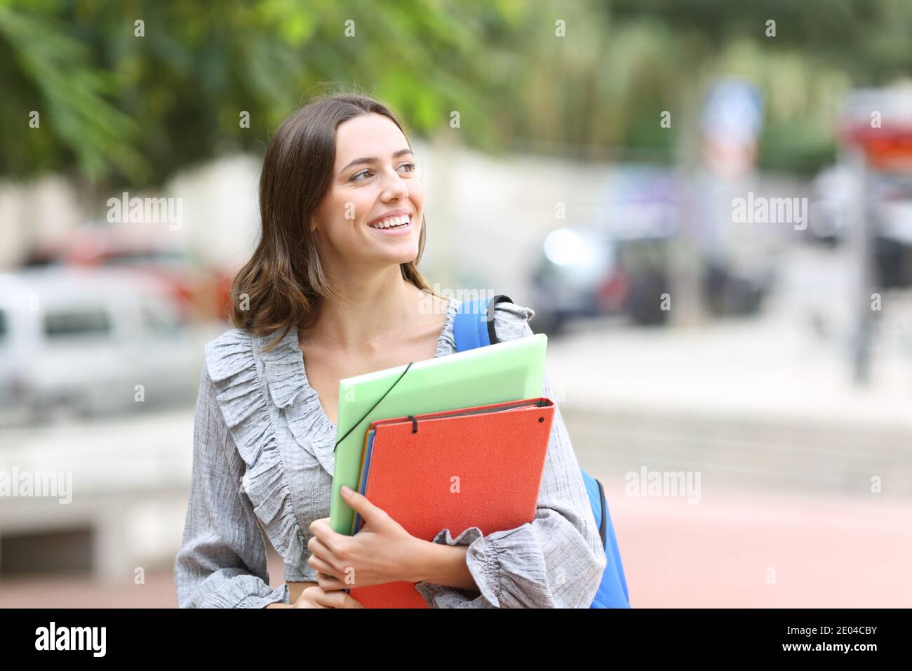Happy student walking towards camera looking at side in the street Stock Photo