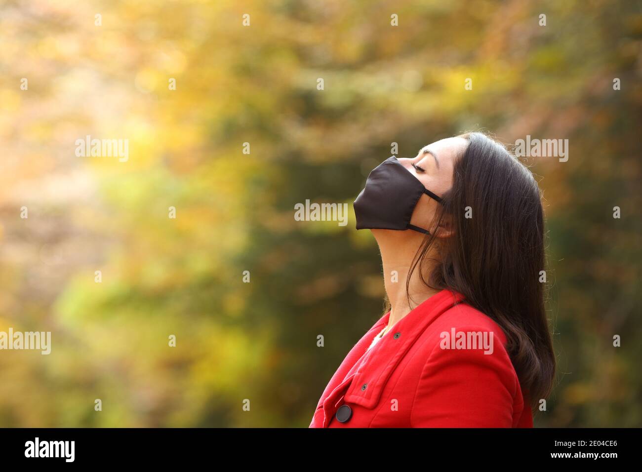 Side view portrait of a woman in red breathing fresh air with mask in a forest in covid times Stock Photo