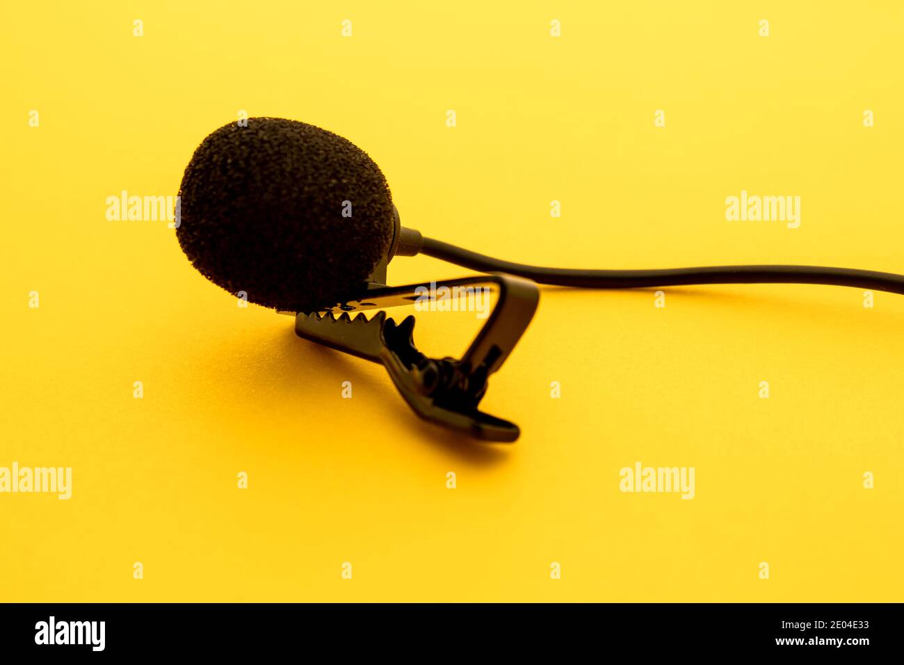 Lavalier or lapel microphone on a yellow surface, very close-up. The details of the grip clip or bra and the sponge against the wind are visible. Stock Photo