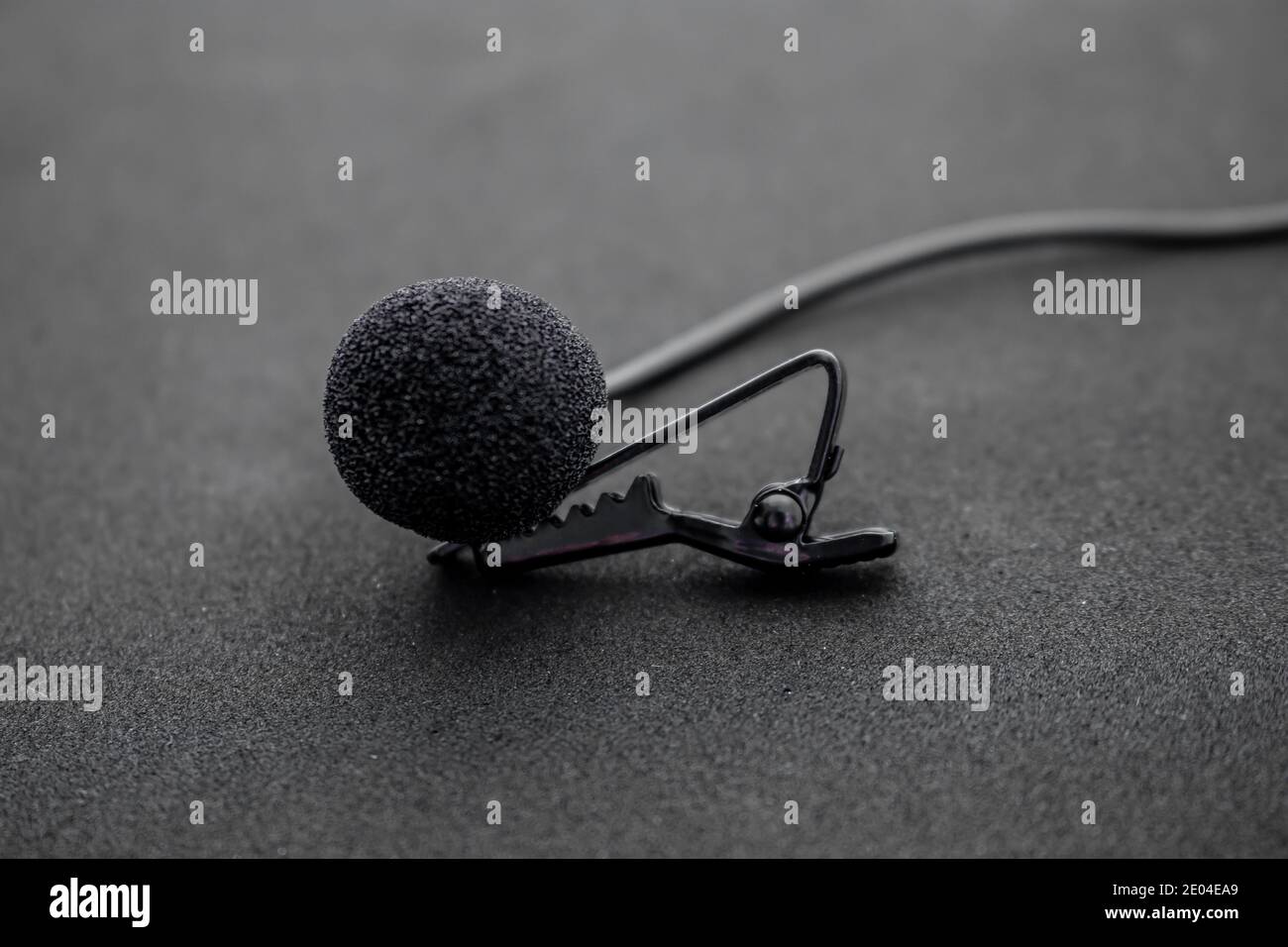 Lavalier or lapel microphone on a black surface, very close-up. The details of the grip clip or bra and the sponge against the wind are visible. Stock Photo