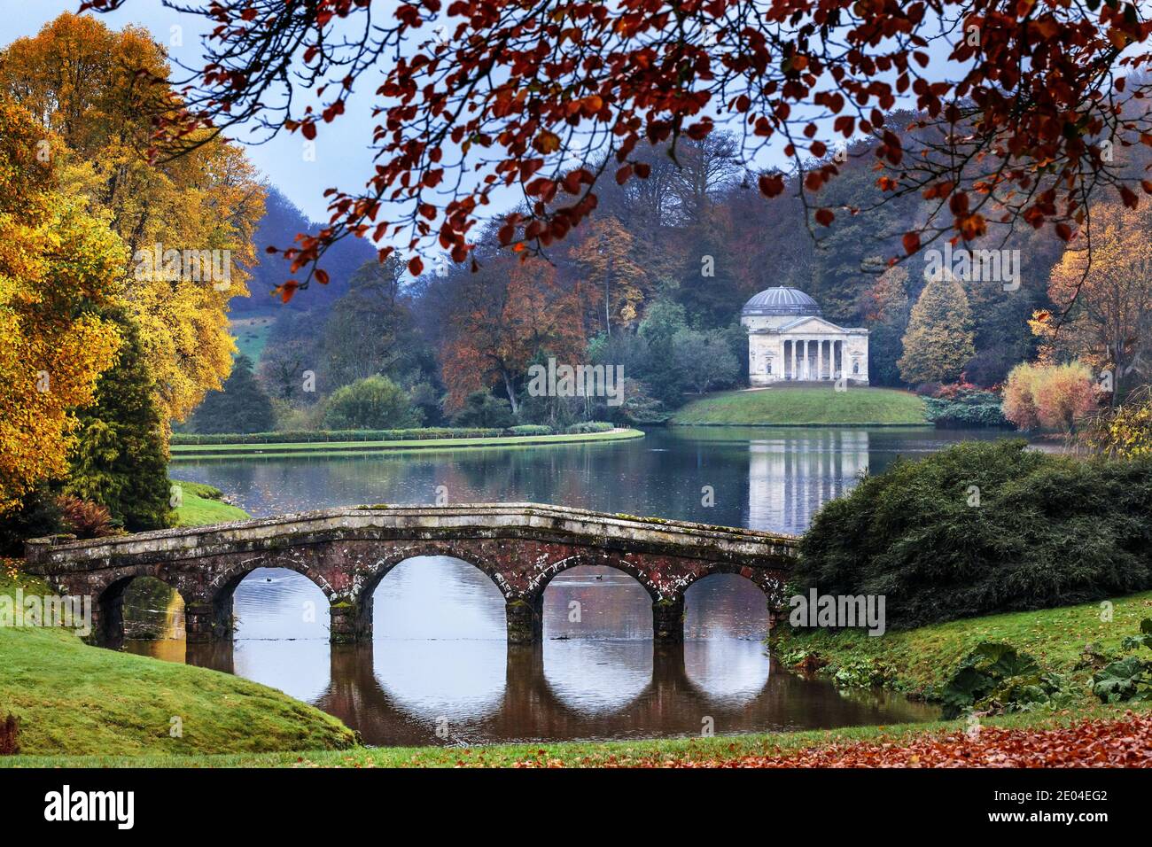 The five arch Palladian bridge with the Pantheon in the distance at Stourhead in Wiltshire, England. Stock Photo