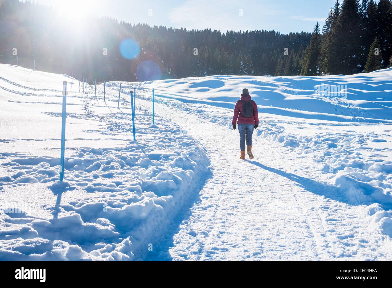 Lonely woman walking along a snow covered path in the mountains on a sunny winter day. Lens Flare. Stock Photo
