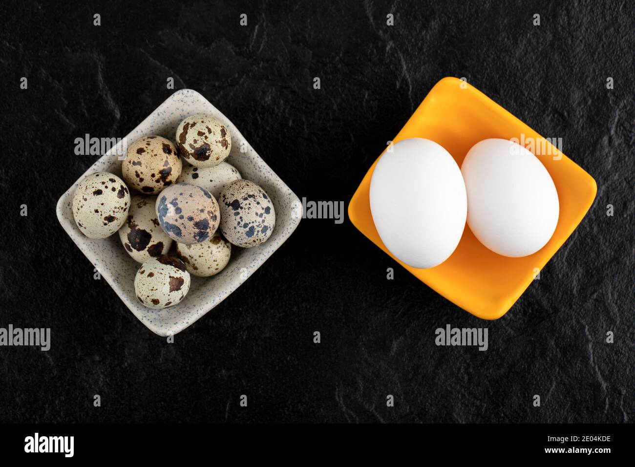 Three quail eggs and chicken eggs on black background Stock Photo