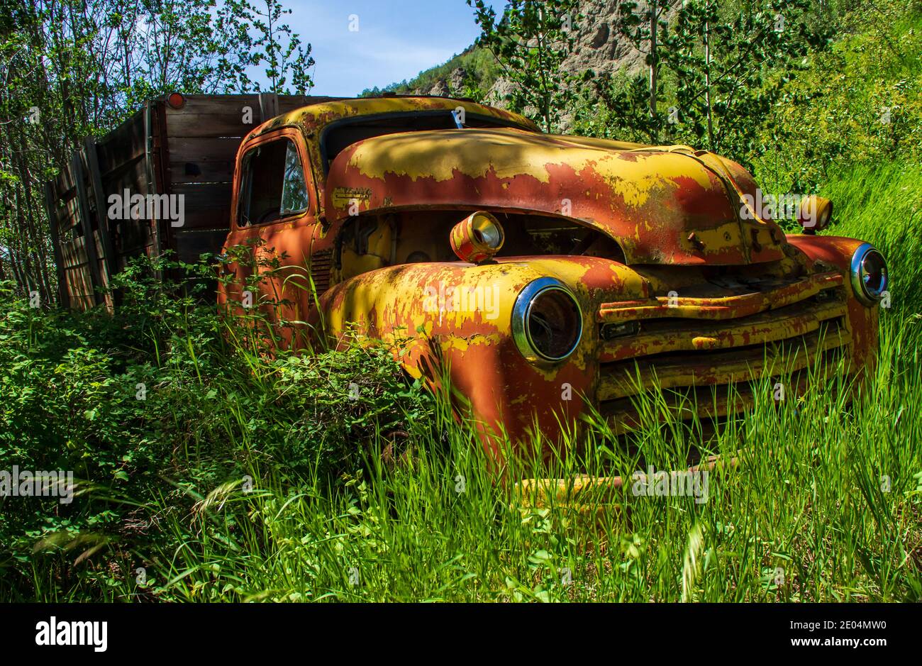 Old truck with peeling yellow paint and rust, abandoned in tall grass at Telegraph Creek in the Stikine Canyon in northern British Columbia. Stock Photo