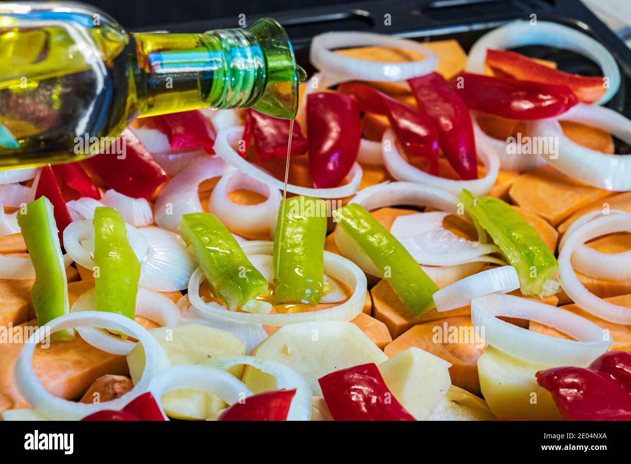Bottle pouring olive oil on raw chopped vegetables placed on a oven tray Stock Photo