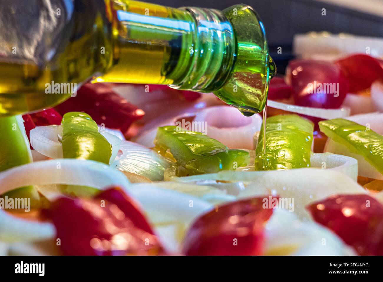 Close up of bottle pouring olive oil on raw chopped vegetables placed on a oven tray Stock Photo