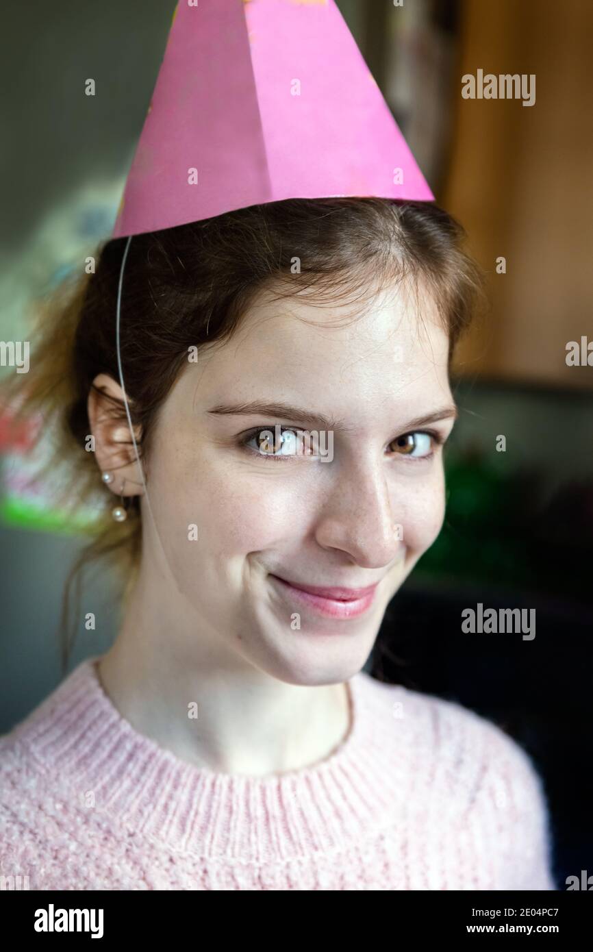 Portrait of a cute young woman wearing a birthday cone looking camera, indoors Stock Photo