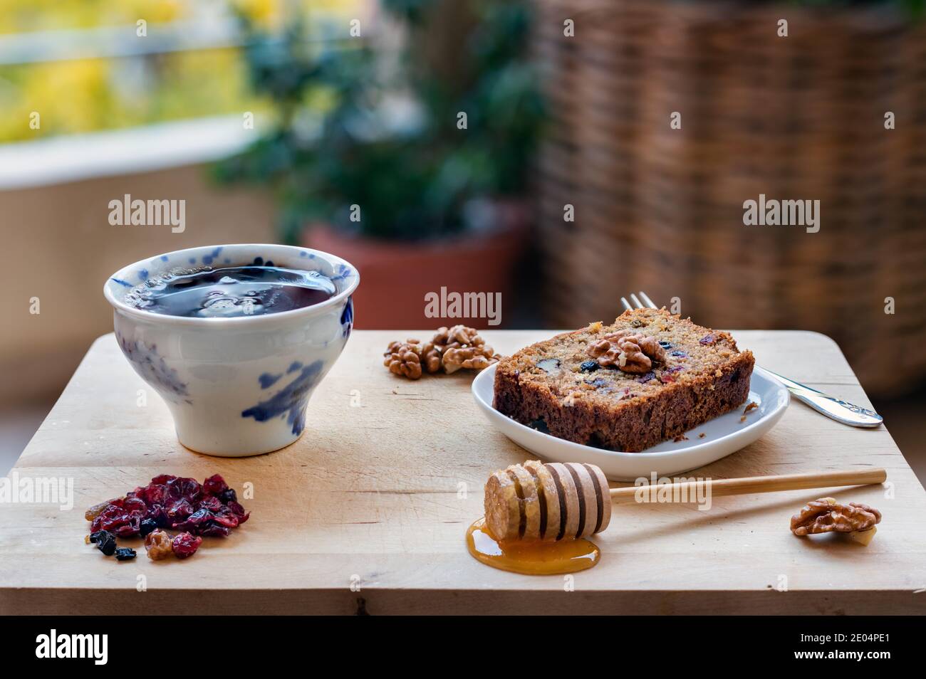 A slice of vegan cake with super fruit and nuts, honey and a cup of tea on wooden table Stock Photo