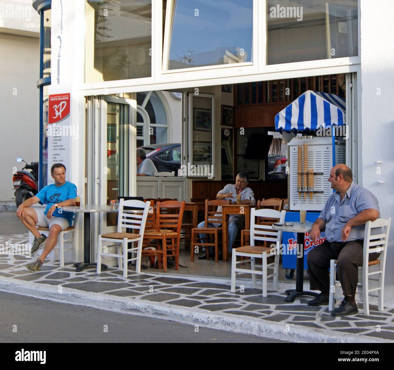 Men sit inside and outside a Greek cafe in Naxos, Greece. Stock Photo