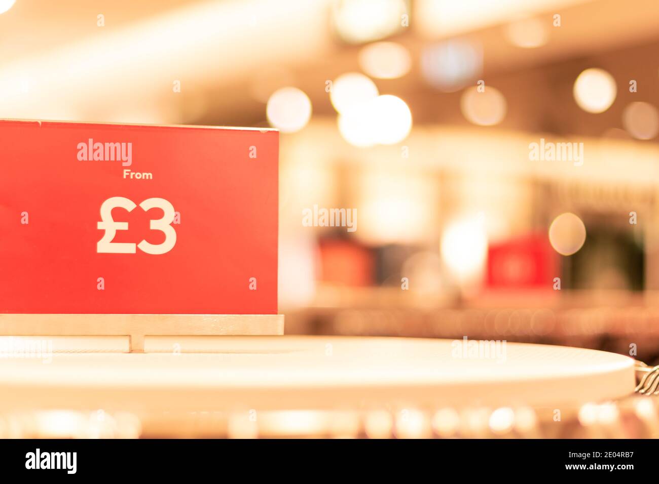 Oxford, UK -14 Dec 2020: Red Sale price tag closeup in Hennes and Mauritz AB store, prices from three pounds sign, blurry background behind the sign Stock Photo