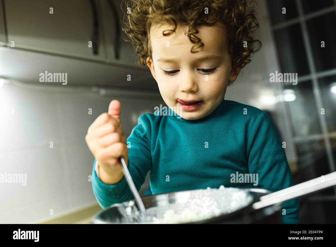 Little curlyhaired girl plays cooking in a real kitchen with natural