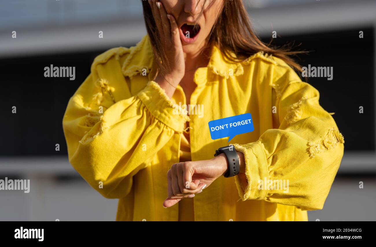 Young forgetful woman checking message on a smartwatch and feels shocked because she forgot about a meeting. Woman being late Stock Photo