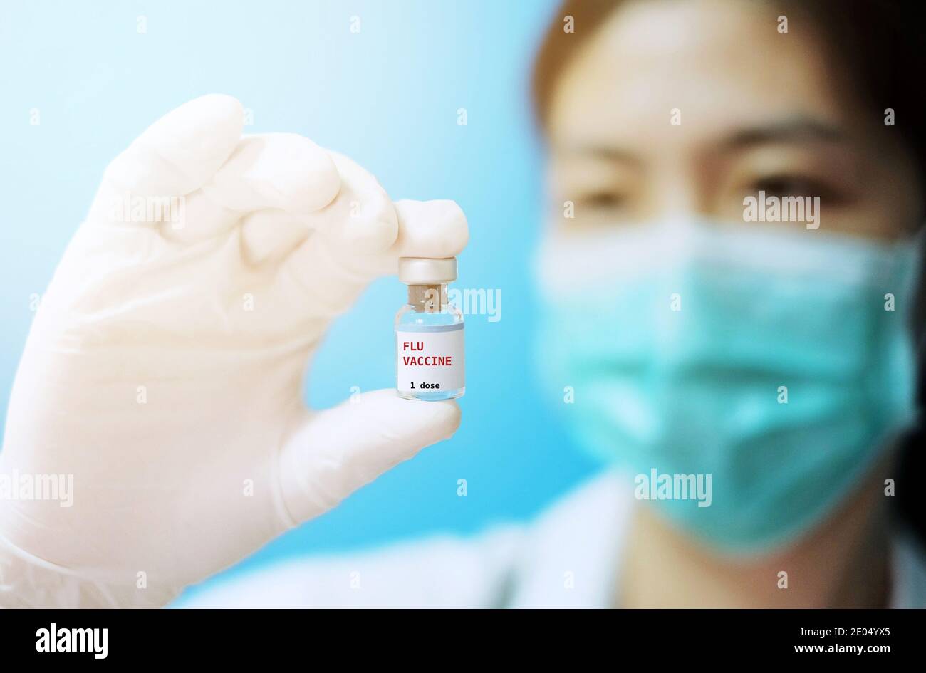 A female Asian physician with surgical mask and white rubber gloves at a clinic, holding a glass bottle of 1 dose Flu vaccine with white background an Stock Photo