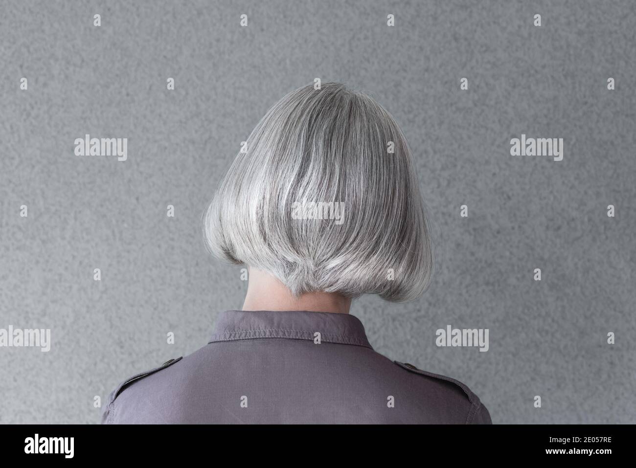 Silver-haired mature lady on gray background, from behind. Stock Photo