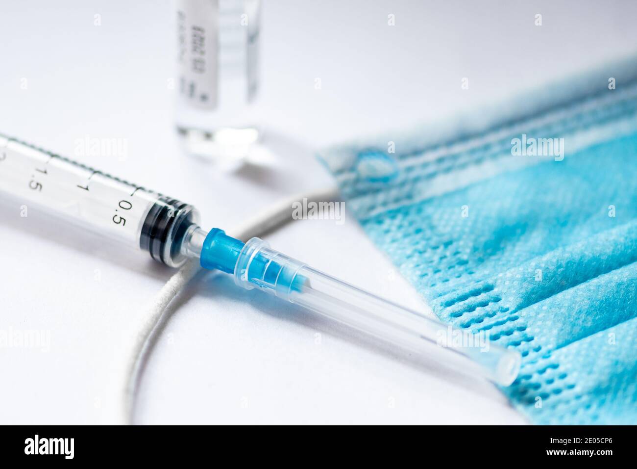 Syringe, vial and surgical face mask on a table ready to be used. Covid or Coronavirus vaccine background Stock Photo
