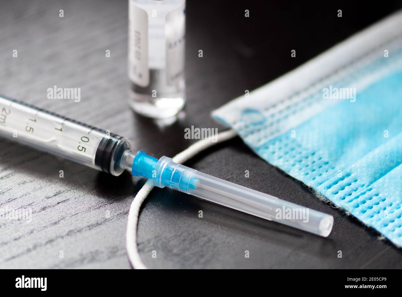Syringe, vial and surgical face mask on a table ready to be used. Covid or Coronavirus vaccine background Stock Photo