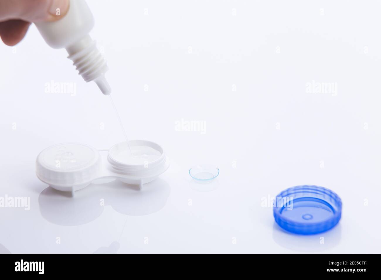 hand adding solution in contact lenses case on white background. Stock Photo