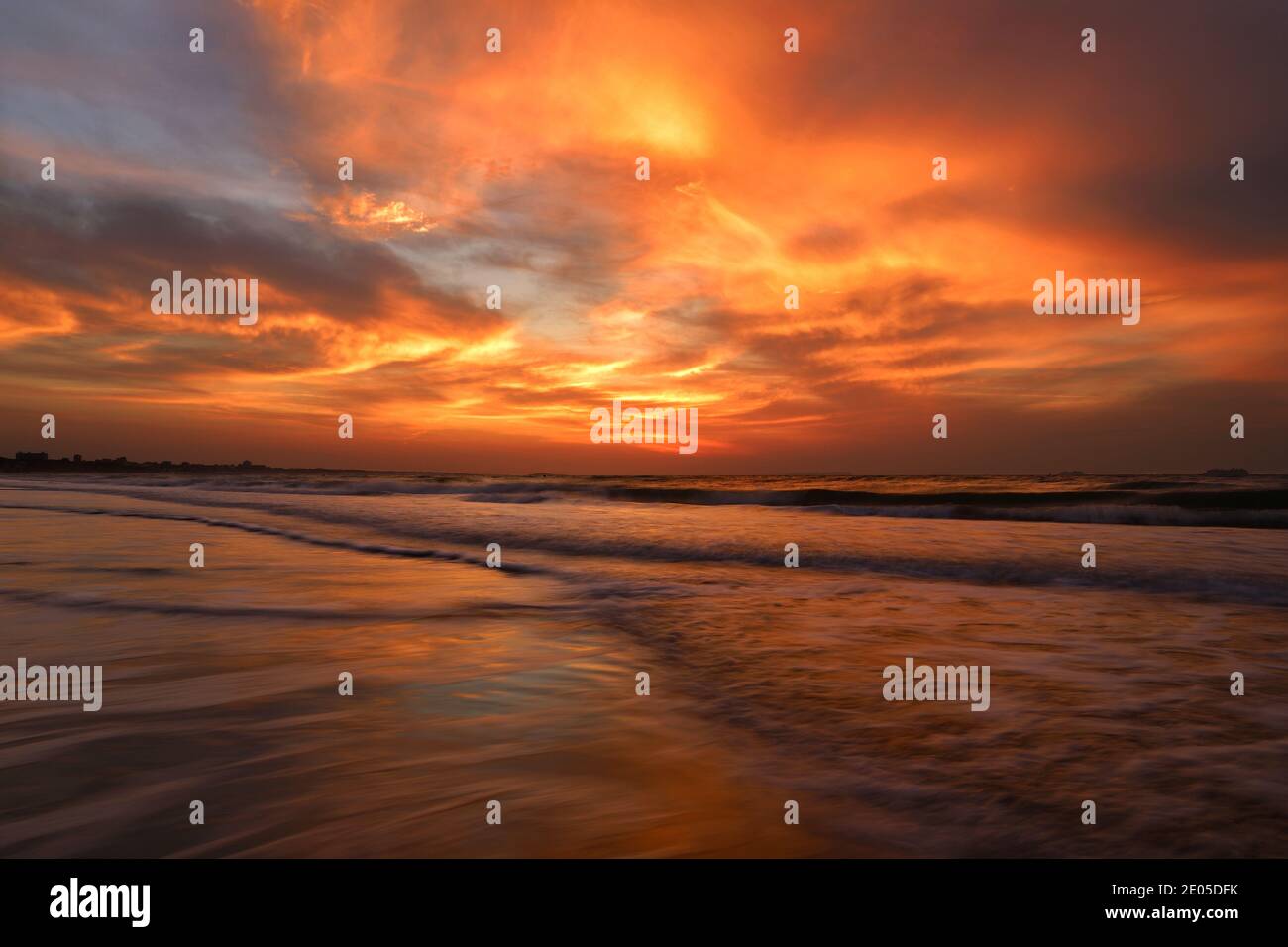 The rising sun sets fire to the cloud filled sky as waves roll over Bournemouth's award winning beach below. Stock Photo