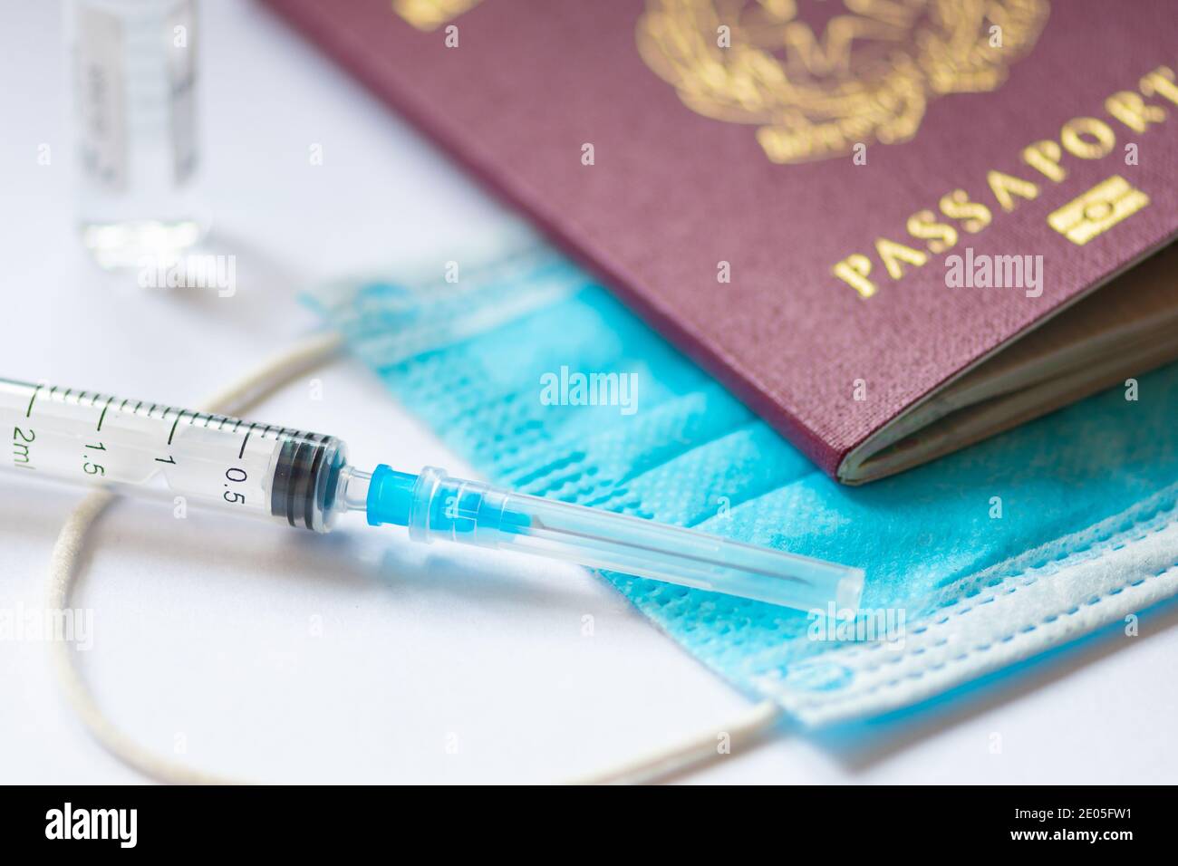 Syringe with needle, vial, surgical face mask and passport or visa on the table ready to be used. Covid or Coronavirus vaccine background Stock Photo