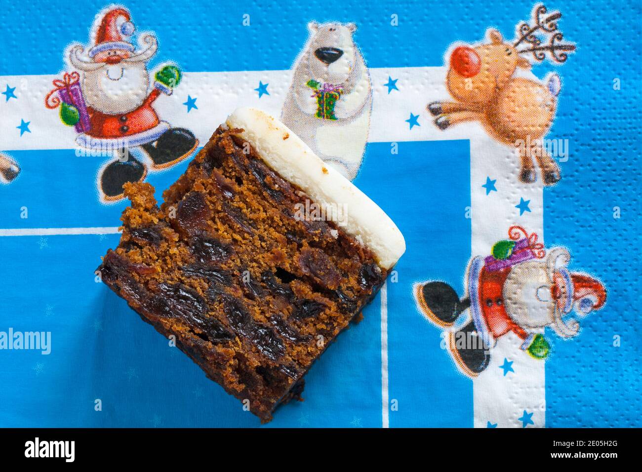 Slice of M&S Iced Fruit Cake Christmas Cake set on blue Christmas serviette napkin - UK festive Xmas Stock Photo