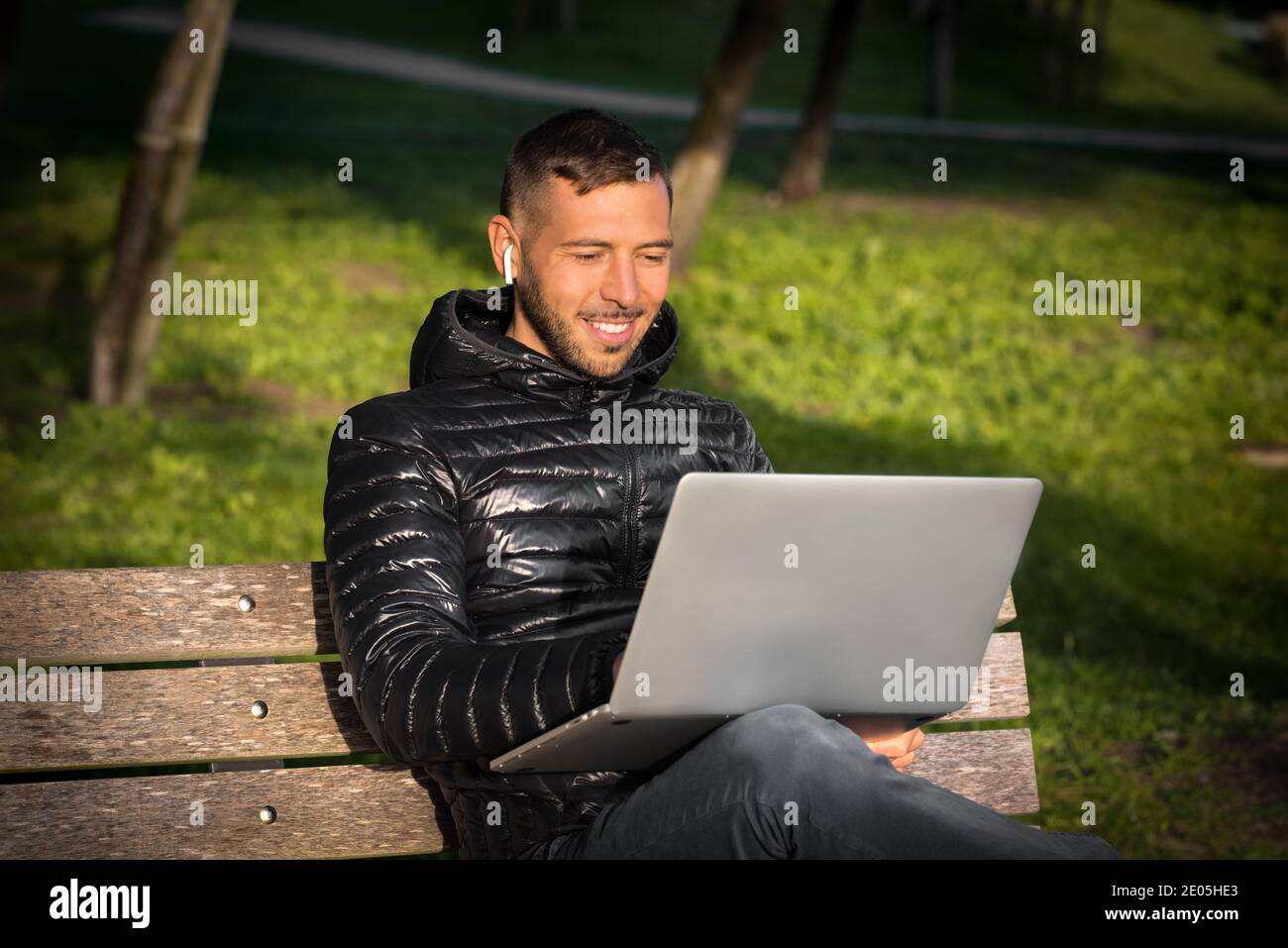 Young man working with laptop and headphones in the city park. Student studying outside. Freelance working concept Stock Photo