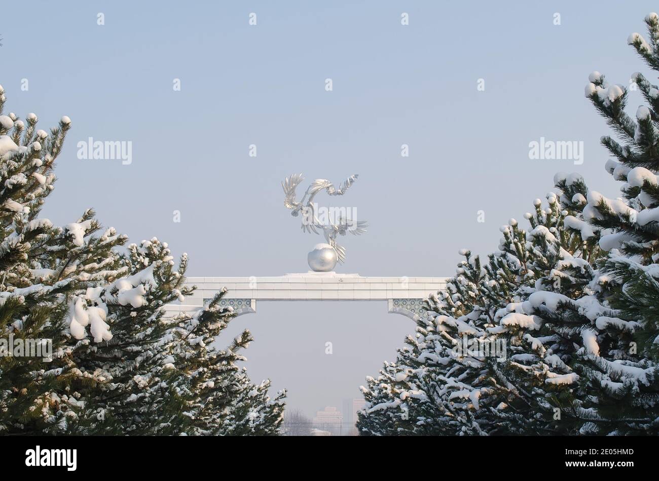 Alley of Christmas trees and arch with three cranes and a globe covered with snow in winter, on Independence square in Uzbekistan Stock Photo