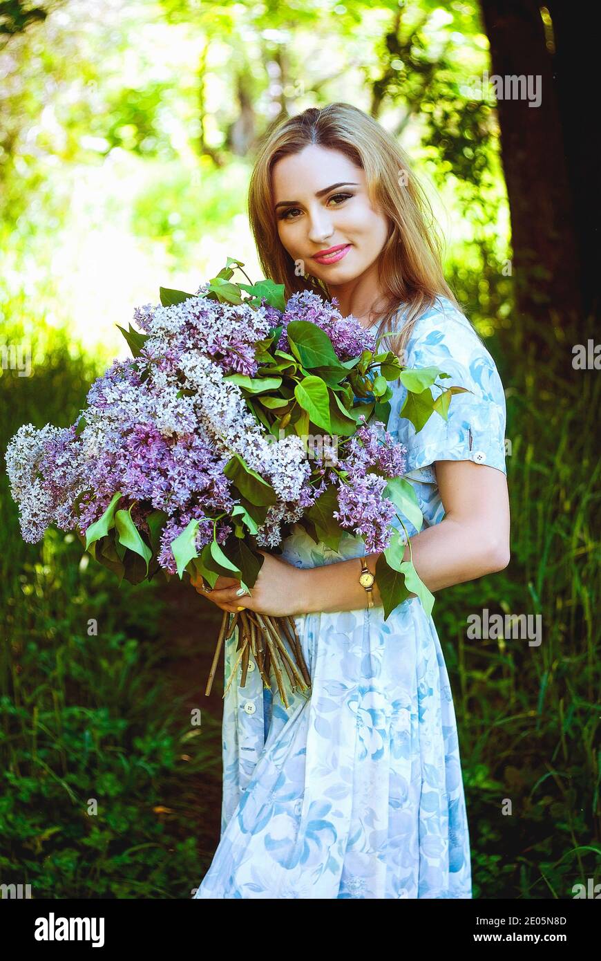 Portrait of young attractive woman in spring garden with a bouquet of lilacs. Spring background. Woman's Day. Greeting card. Stock Photo