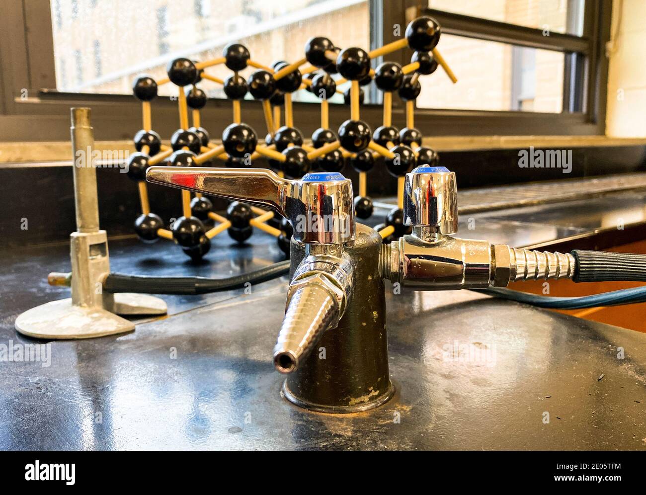 A close up of a Bunsen burner on black lab desk in high school classroom with a model of a