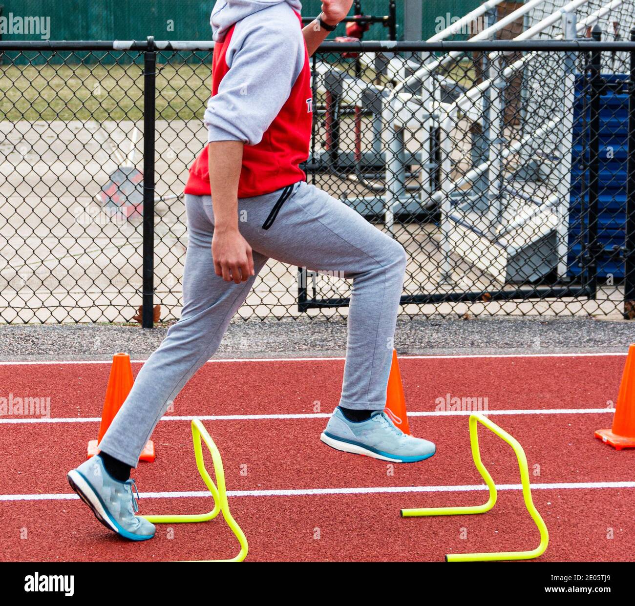 A high school track and field biy is running over yellow mini hurdles on a red track. Stock Photo