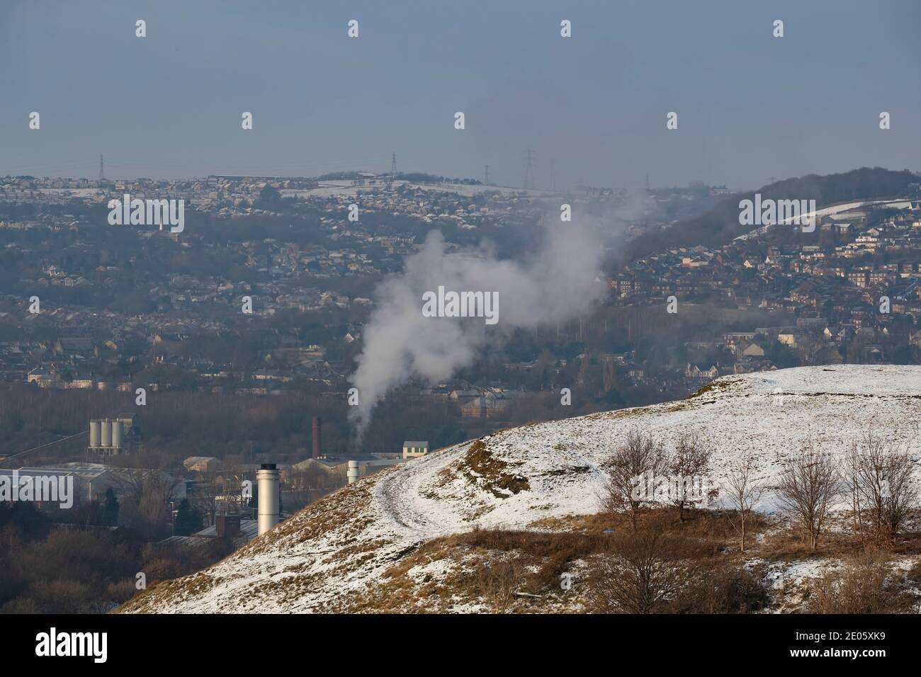 Smoke rising in the still winter's air from an industrial plant in Huddersfield as winter snow covers the gloomy landscape Stock Photo