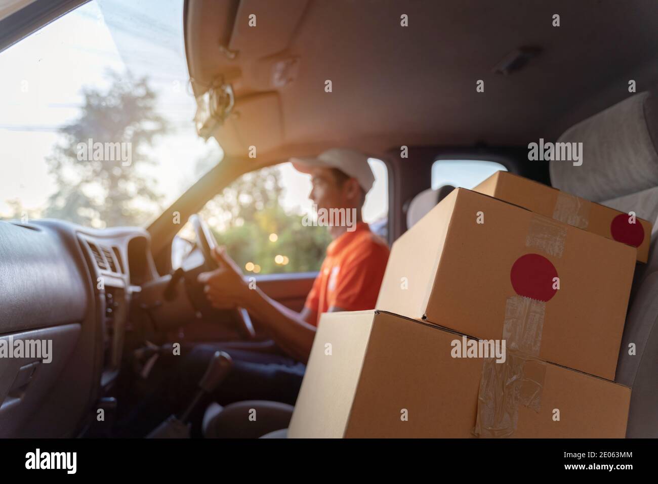 Asian delivery driver driving van with parcels on seat outside warehouse. Land transport concept. Stock Photo