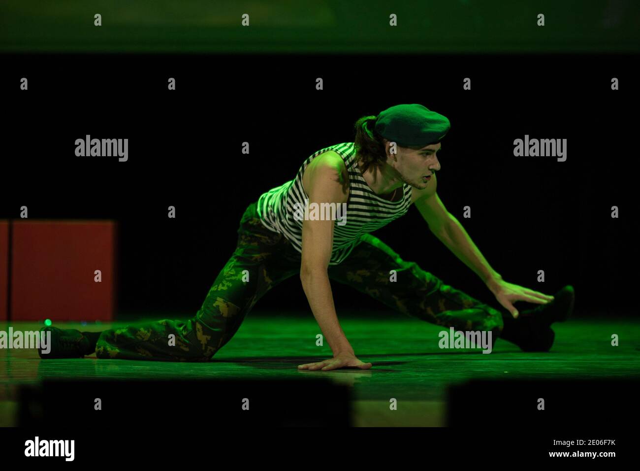 A young guy in military uniform is dancing on stage in a stage light. Stock Photo