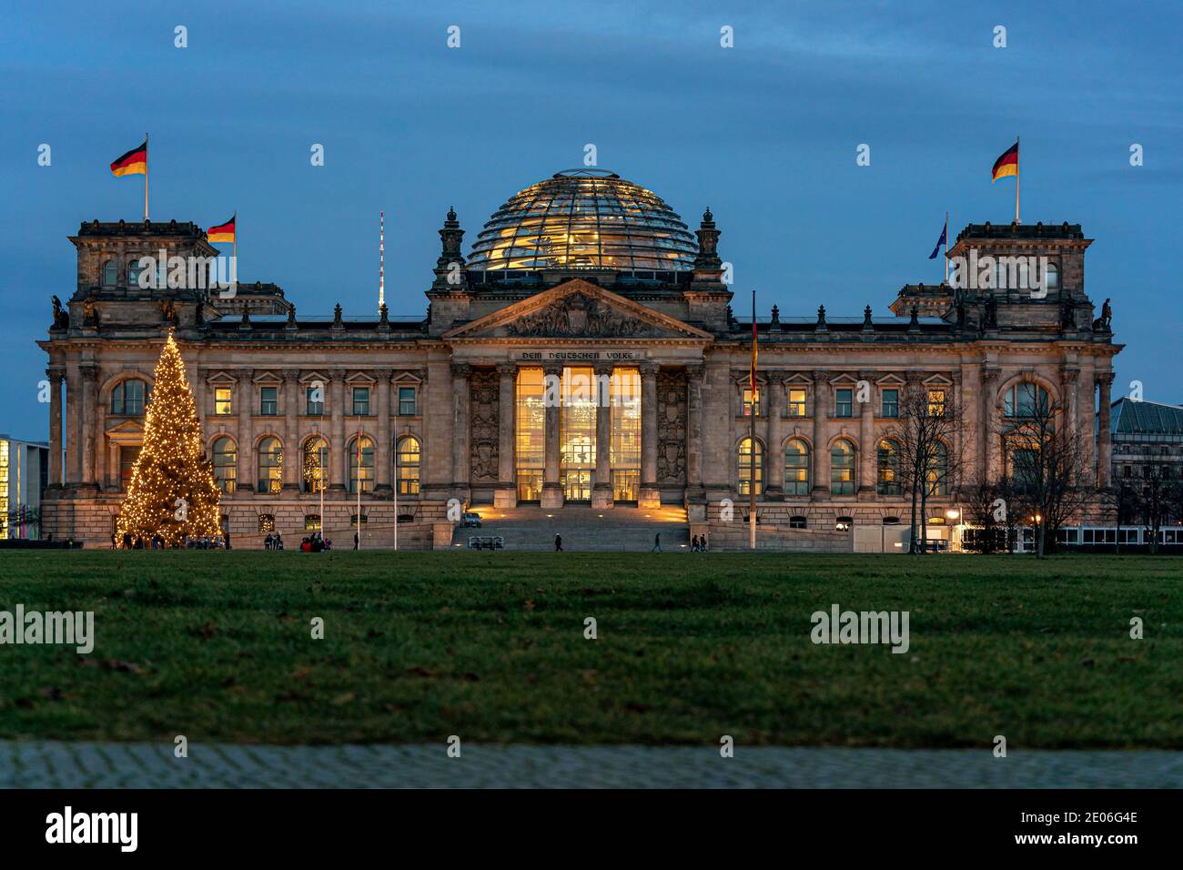 December 28, 2020, the Berlin Reichstag building by master builder Paul Wallot on Platz der Republik with flags and Weihaftertsbaum, illuminated in the evening at blue hour. Front of the building with the lettering 'Dem Deutschen Volke'. The Reichstag is the seat of the German Bundestag with plenary area. | usage worldwide Stock Photo