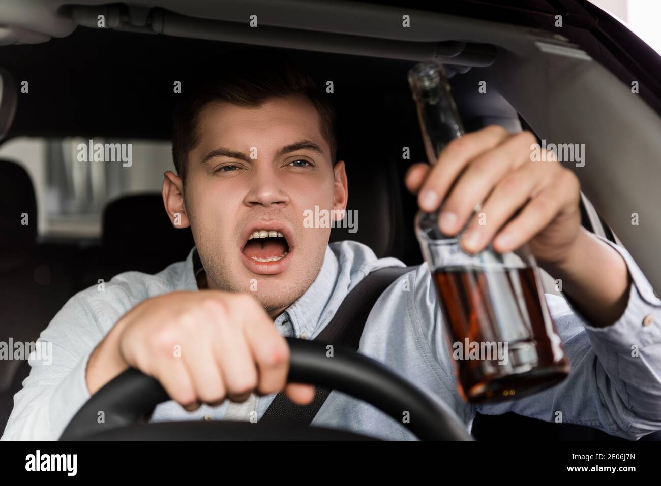 drunk, aggressive man shouting while driving car and holding bottle of