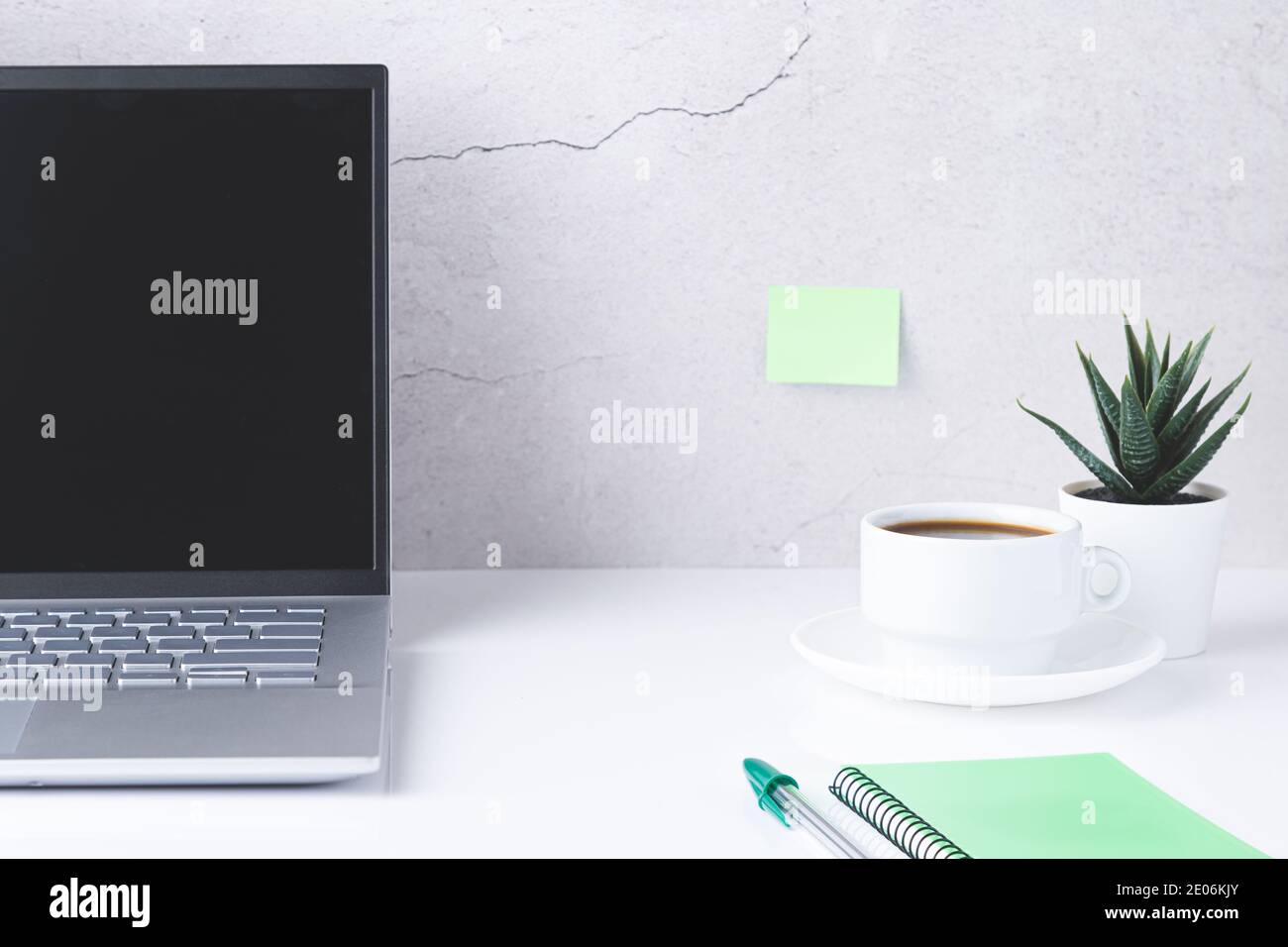 White desk with laptop,  cup of coffee and green notebook and pen. Stock Photo