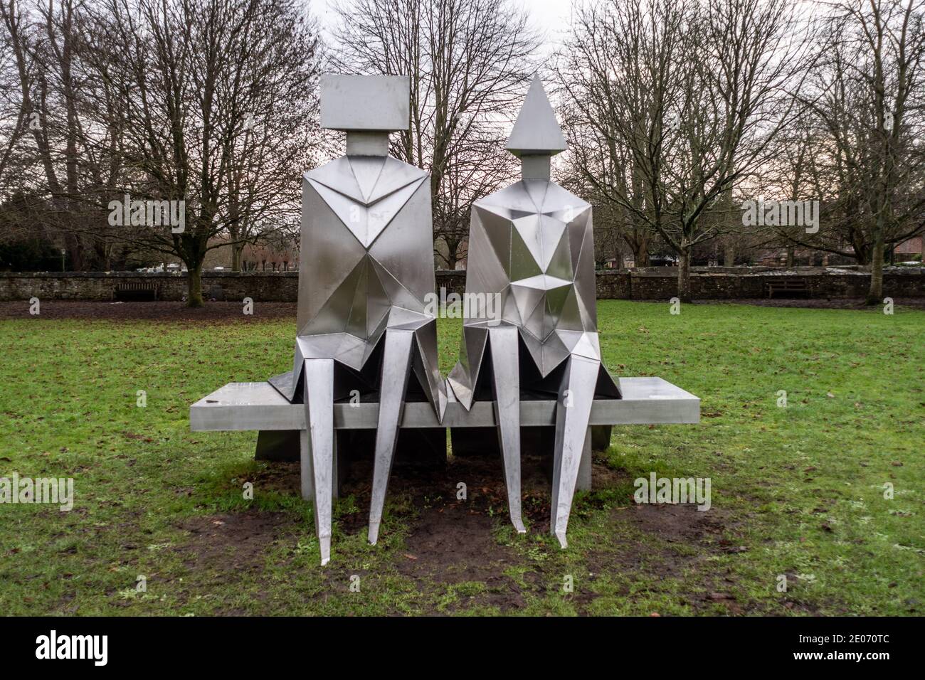 Stainless Steel sculpture by Lynn Chadwick entitled 'Sitting Couple on Bench' in the grounds of Salisbury Cathedral, Wiltshire, UK Stock Photo