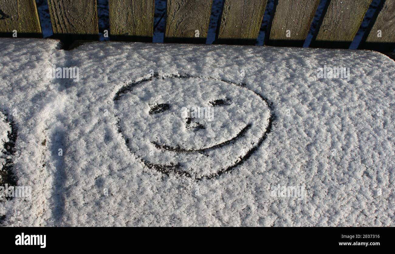 Smiley face drawn in fresh snow. Winter gardens in the United Kingdom (UK). Winter seasons and happy emotions. Happy face in snow next to garden fence Stock Photo