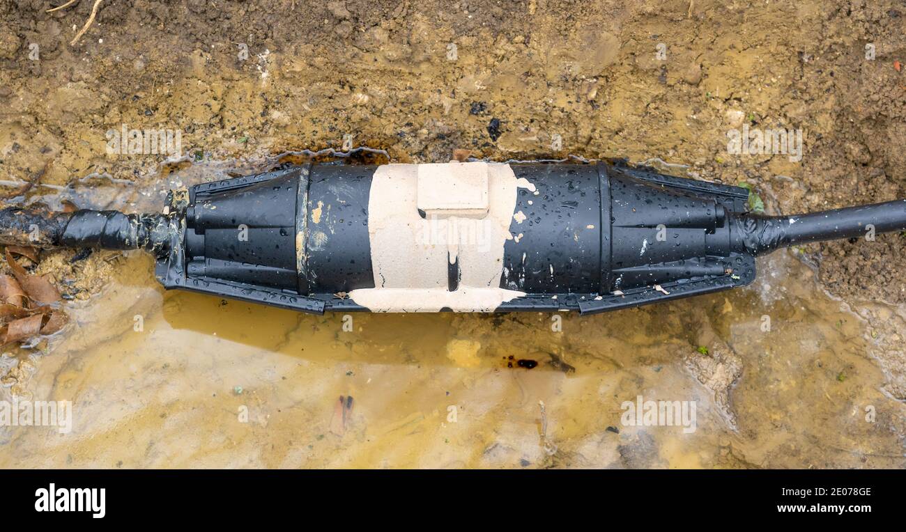 Close up of a newly installed, sealed resin filled underground straight cable joint in a freshly dug muddy trench. Hertfordshire. UK Stock Photo