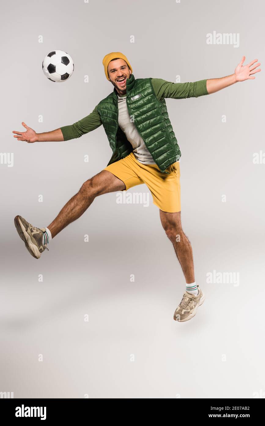 Positive man jumping near football in air on grey background Stock Photo