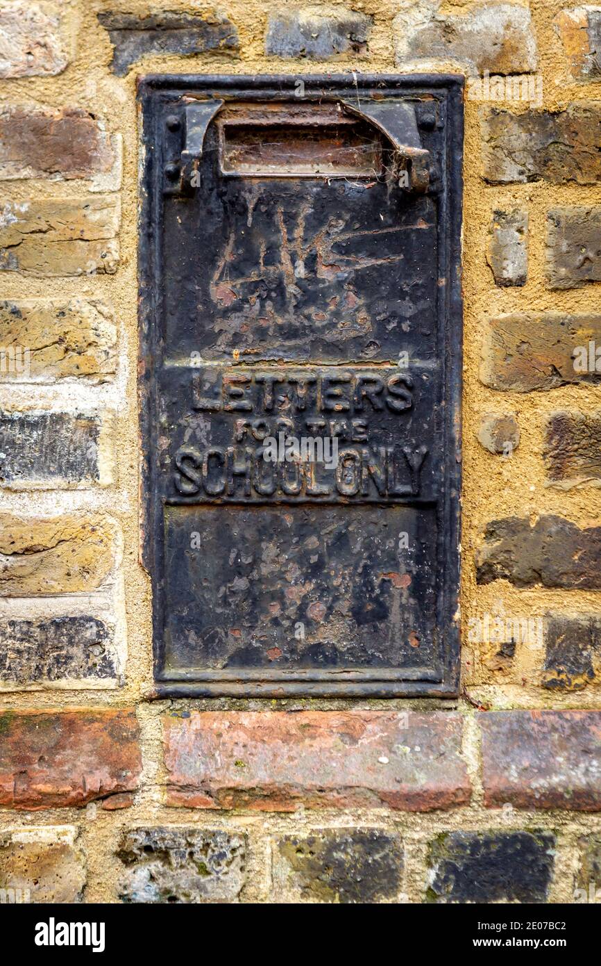 Built into the brick wall next to the school is an old black letterbox Stock Photo