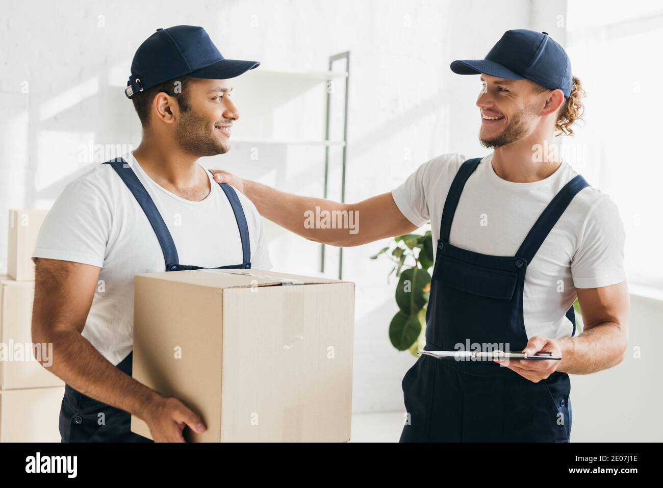 cheerful multicultural movers smiling while looking at each other in apartment Stock Photo