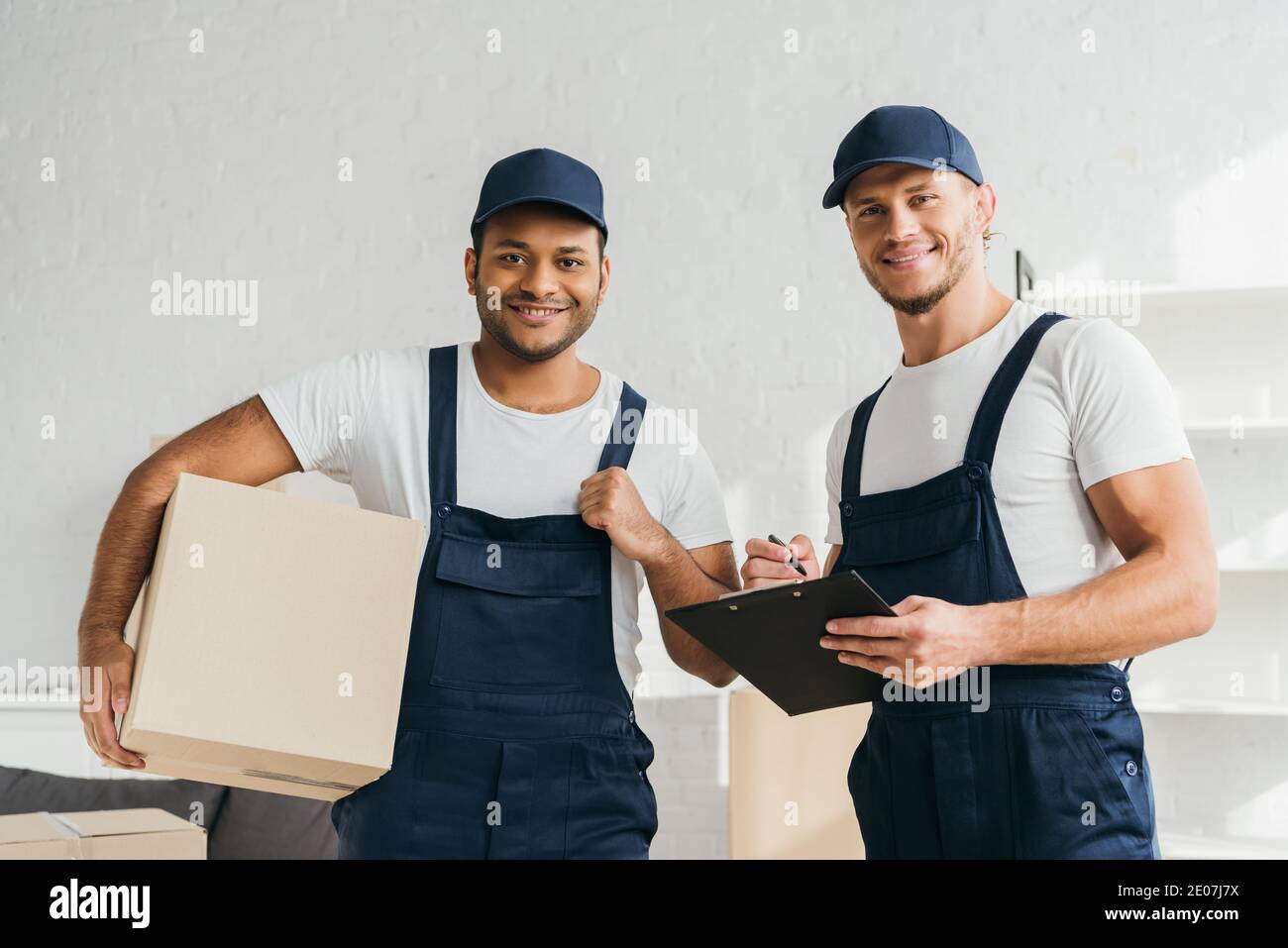 cheerful multicultural movers smiling while looking at camera in apartment Stock Photo