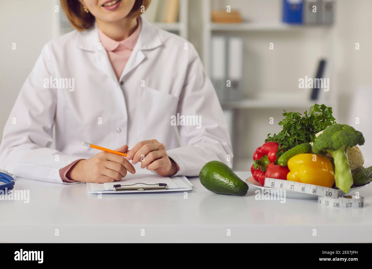 Dietitian sitting at table with fresh fruit, vegetables and individual diet plan Stock Photo
