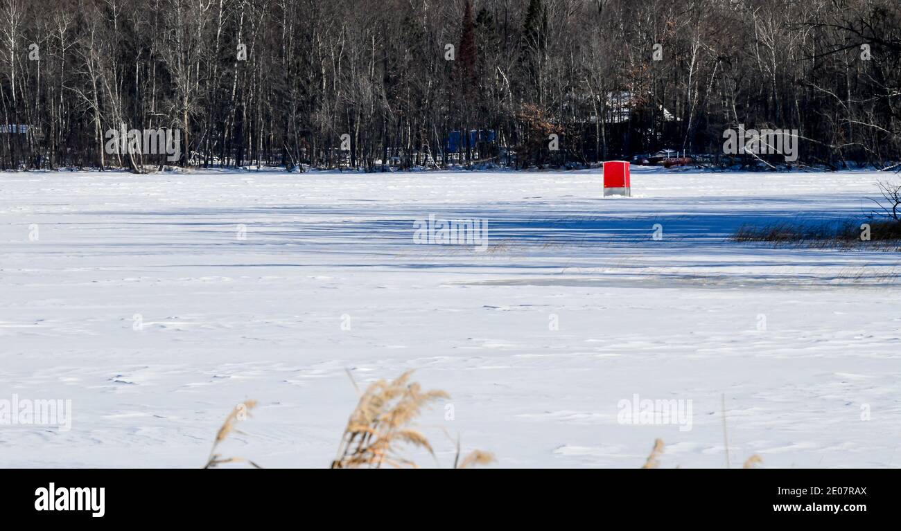 Little red ice fishing shanty on the frozen lake with snow and blue sky Stock Photo