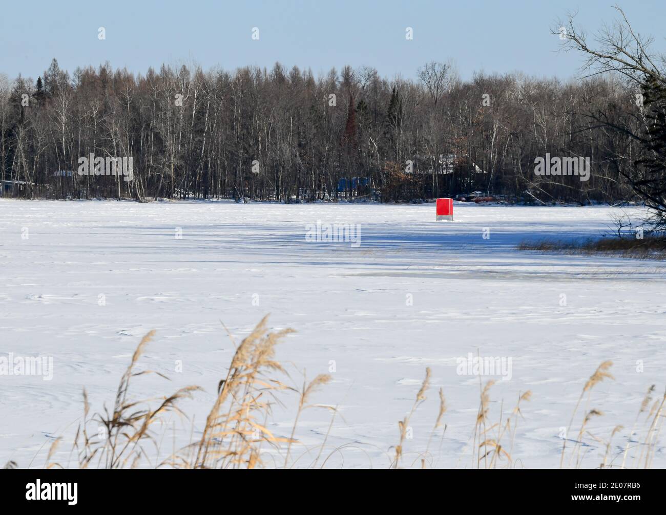 Little red ice fishing shanty on the frozen lake with snow and blue sky Stock Photo