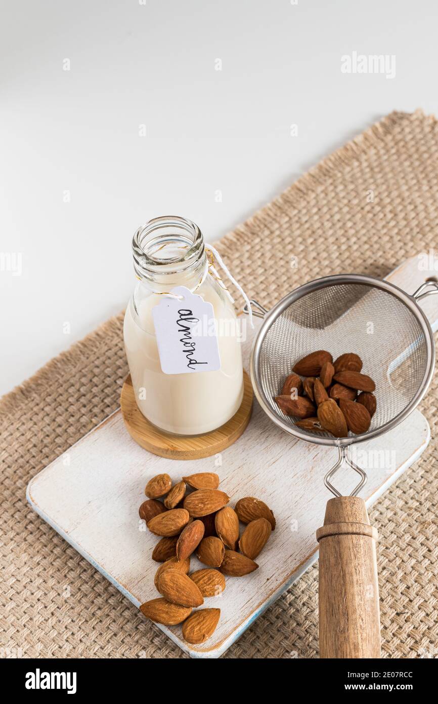 Almond milk tagged in a bottle next to a strainer full of almonds and a  bunch of them. Vertical view Stock Photo - Alamy