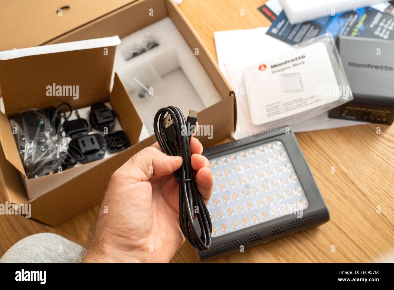 Paris, France - Dec 8 2020: POV male hand unboxing unpacking new USB cable of a Manfrotto LED Light Lykos 2.0, 2 in 1 water-resistant with Bluetooth package in background Stock Photo