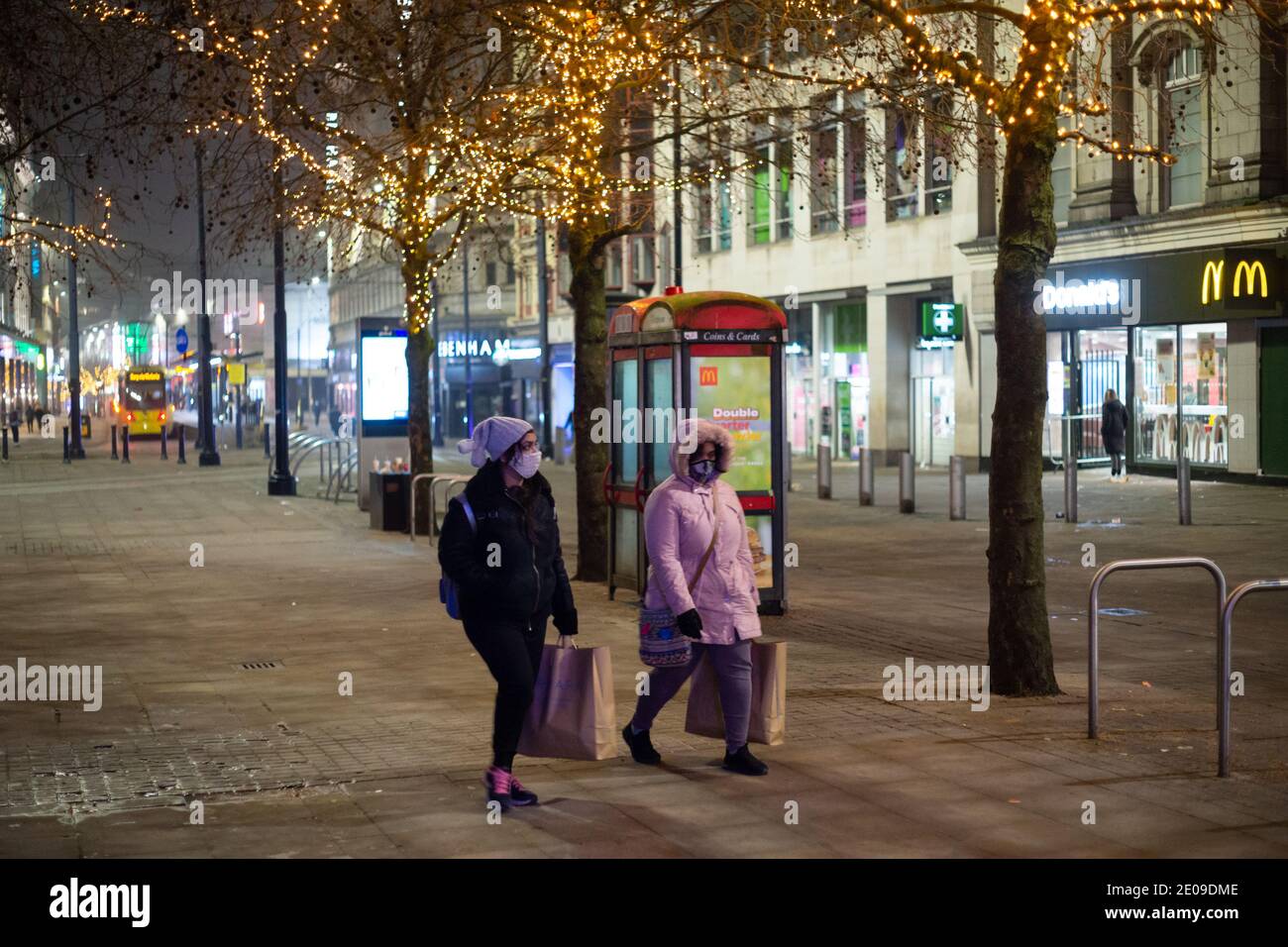 Manchester, England, UK. 30th Dec 2020. Scenes from around Manchester city centre late on the evening of the 30th. At midnight the city will be placed under Tier 4 coronavirus restrictions after a government announcement earlier today. Two women wearing face masks walk up the street carrying shopping bags. Credit: Callum Fraser/Alamy Live News Stock Photo